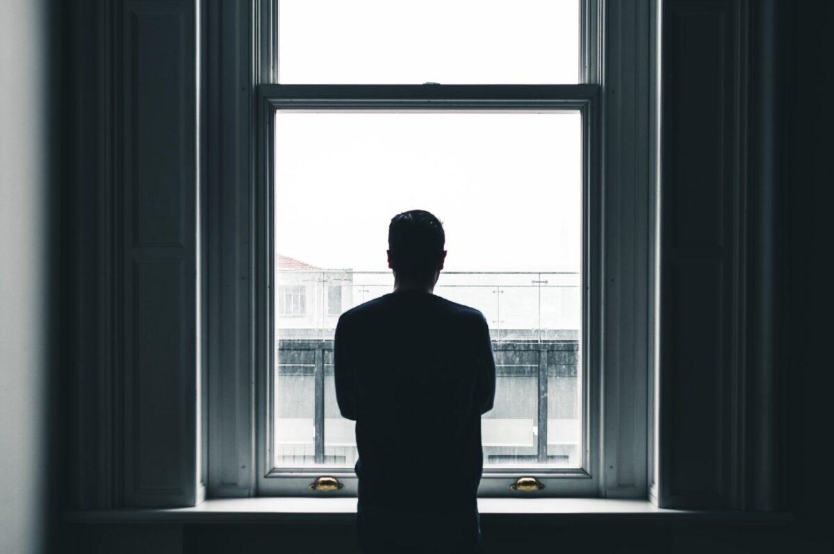 man looking out a window from a dark room