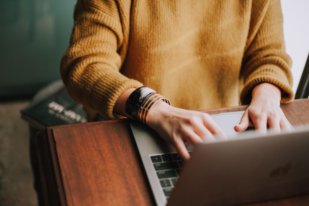 white woman in a yellow jumper typing on a laptop