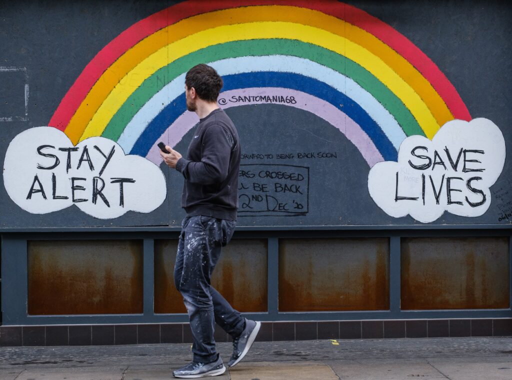 A man walking past street art of a rainbow supporting the NHS