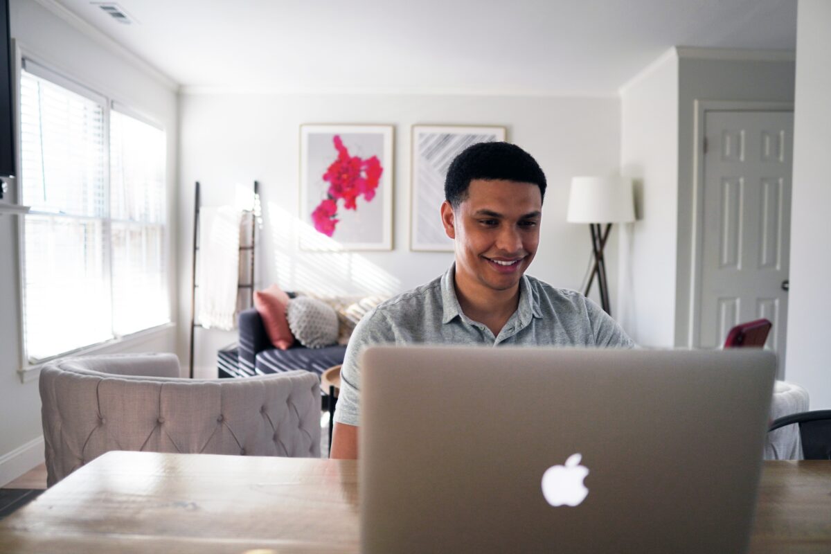 a young man smiling using a laptop at home