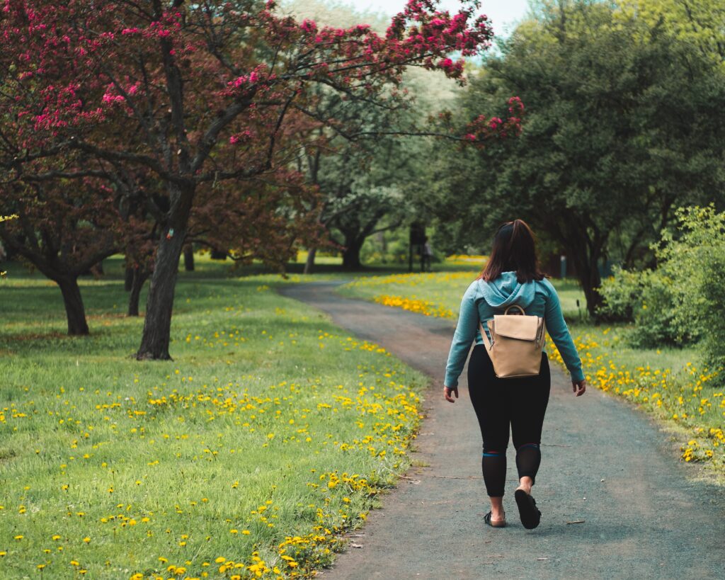 A young dark haired woman walking along a path through a park 