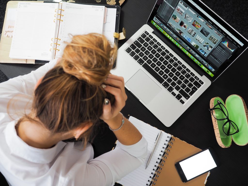 Woman with head in hands with laptop and notebook in front of her